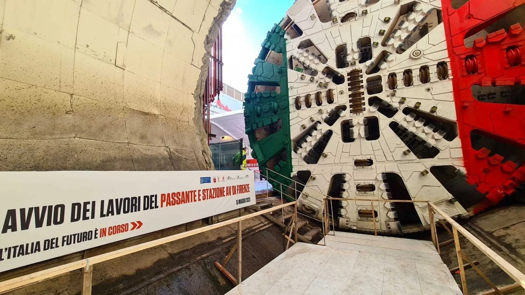 Testa di fresa della TBM con i colori verde, bianco e rosso, accanto al cartello dell’avvio dei lavori del Passante AV di Firenze